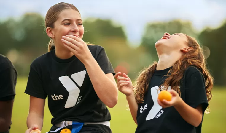 2 girls laughing and eating oranges