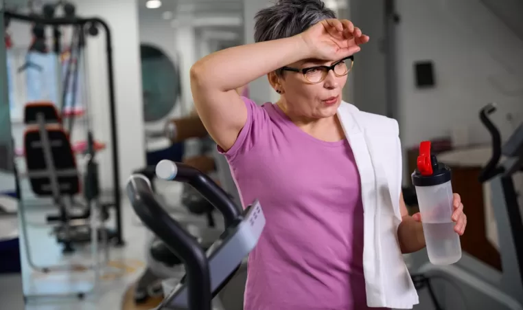 Mature tired woman wearing sportswear with bottle of water wiping her forehead